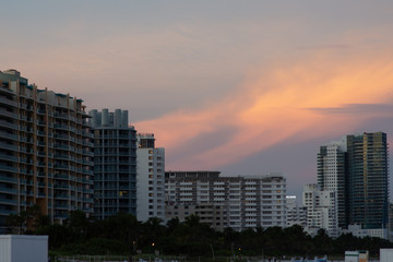 Fototapeta na wymiar Sunset paints warm pink colors across the blue sky above tall buildings at the beach one evening