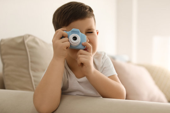 Little photographer taking picture with toy camera on sofa at home