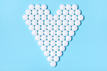Heart made of white round pills on a blue background. Medical, pharmacy and healthcare concept. Top view
