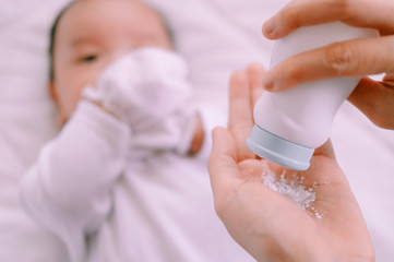 Mother preparing baby powder in her hand and 2 months old baby boy on bed.