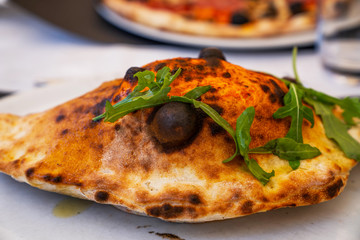 Baked calzone on the plate. Closed type of pizza, decorated with basil twigs on a restaurant table background.