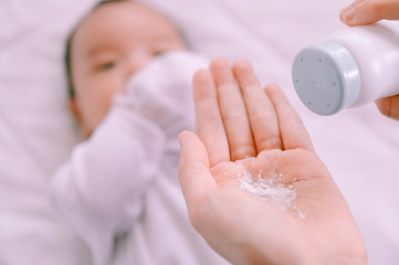 Mother preparing baby powder in her hand and 2 months old baby boy on bed.