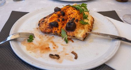 Baked calzone on the plate. Closed type of pizza, decorated with basil twigs on a restaurant table background.