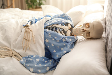 Human skeleton in pajamas lying on bed indoors