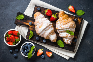 Croissant with fresh berries and cup of coffee on black.