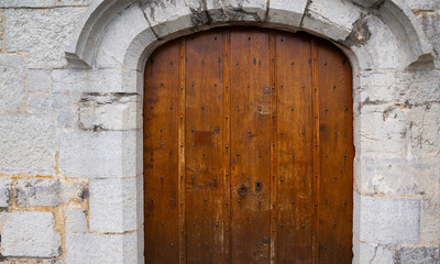 Fototapeta na wymiar Medieval castle gate. Ancient wooden door in old stone castle wall. Locked wooden door with metal forging.