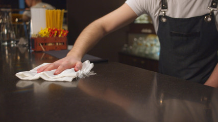 Bartender in the apron wipes bar counter with a rag, close up