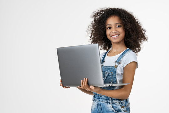 Portrait of little girl holding laptop computer while standing and looking at camera isolated over white background