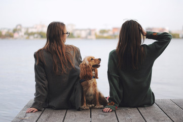 Two girls and english cocker spaniel dog lying on wooden bridge.Portrait of dog outside (outdoors). Sunny day.