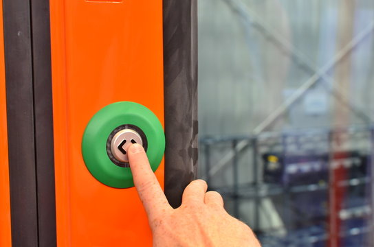 The hand presses the button for stop in the train. Orange door of train carriage with the electric blue button press to open sliding mechanical door at a train station platform.