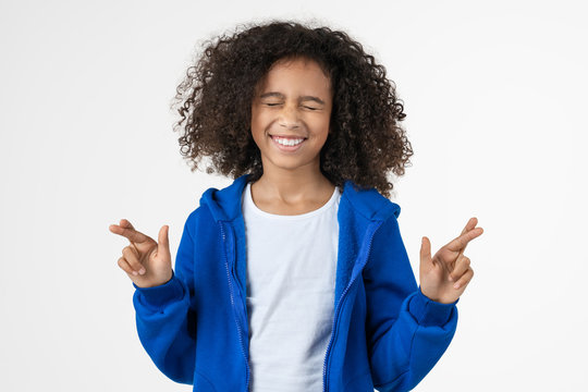Cheerful little african girl holding fingers crossed for good luck standing isolated over white background