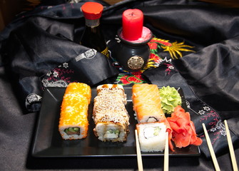 Sushi is a Japanese dish that consists of glutinous rice with fish, seafood and vegetables. On a black background is a plate with sushi, ginger, soy sauce and wasabi, wooden sticks.
