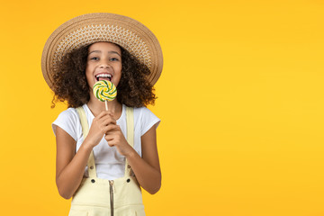 Cute young african girl kid eat candy isolated over yellow background