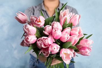 Woman with beautiful pink spring tulips on light blue background, closeup