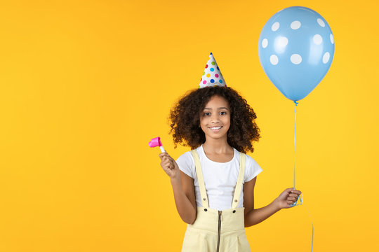 Cute little girl with party hat holding balloon isolated on yellow background