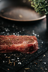 Sirloin steak preparation, seasoning with pepper and salt. Chef preparing fresh meat on dark marble plare.