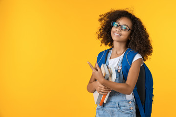 Cute smiling little african american schoolgirl with books on yellow background