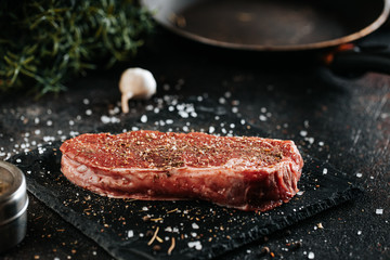 Sirloin steak preparation, seasoning with pepper and salt. Chef preparing fresh meat on dark marble plare.