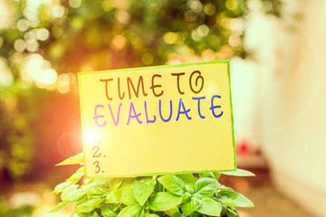 Writing note showing Time To Evaluate. Business concept for judge something with respect to its worth or significance Plain paper attached to stick and placed in the grassy land