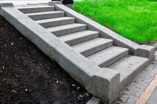 a granite staircase of stone blocks climbing up a slope with soil and green grass in the park nobody, close up side view.