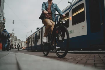 Gardinen Netherlands, Amsterdam, 28 october, 2017: Young hipster guy driving modern black bicycle on cycle track, tram on the background © iana_kolesnikova