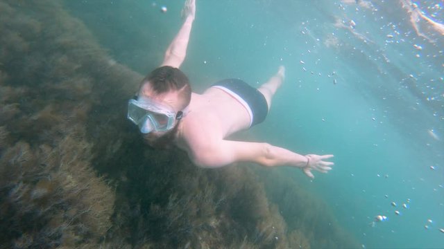 A thin man with a beard in a mask swims underwater, waving his arms. Close-up.