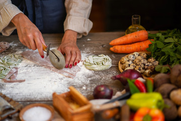 Process of making homemade pasta. Chef make fresh italian traditional pasta. Tasty appetizing classic italian pasta with tomato sauce, cheese parmesan, basil and vegetables on dark table.
