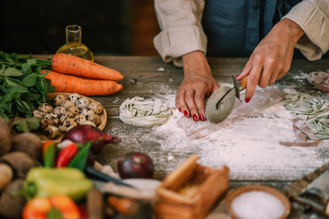 Top view of chef cooking Italian pasta with cheese, vegetables. Italian style pasta on wooden board and ingredients for cooking pasta over dark wood background, top view.