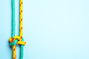 Top view of colorful ropes tied with knot on light blue background, space for text. Unity concept