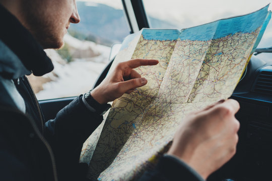 Closeup of traveler hipster man looking on map searching route while sitting in vintage car, lifestyle travel concept, focus on hand, young guy enjoying his vacation in mountains
