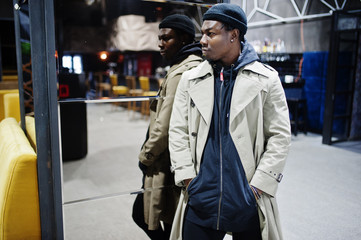 Obraz premium Handsome african american man posing inside night club in black hat and beige coat.