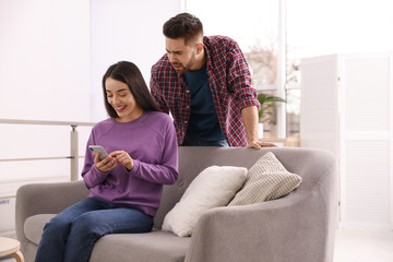 Obraz premium Distrustful young man peering into girlfriend's smartphone at home