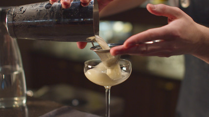 Bartender pours alcohol in glass through a sieve at the bar