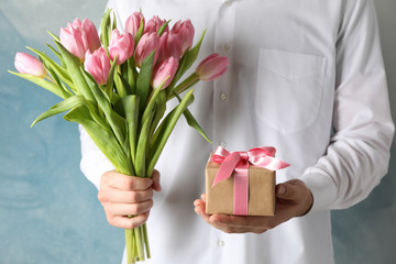 Man holds bouquet of pink tulips and gift on blue background, close up