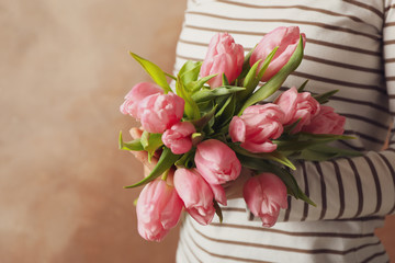 Woman holding bouquet of tulips on brown background, close up