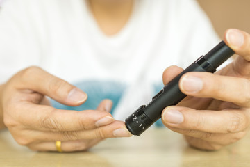 Close up of man hands using lancet on finger to check blood sugar level by Glucose meter. Use as Medicine, diabetes, glycemia, health care and people concept.