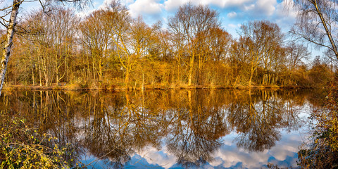 Panorama Spiegelung bunte Bäume und Wolken im See im Winter