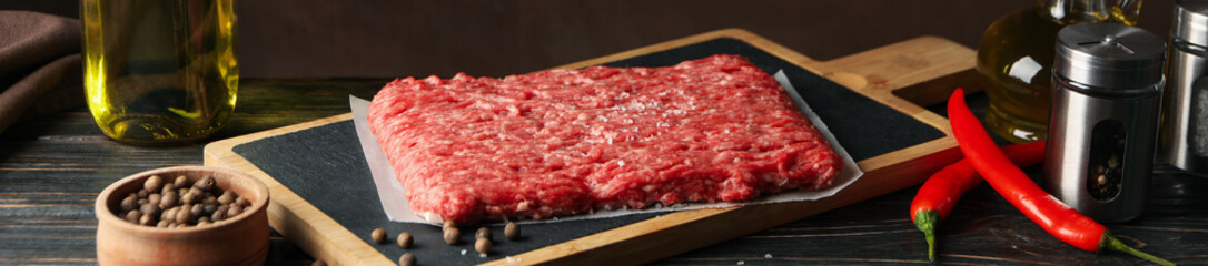 Spices and cutting board with minced meat on wooden background, space for text