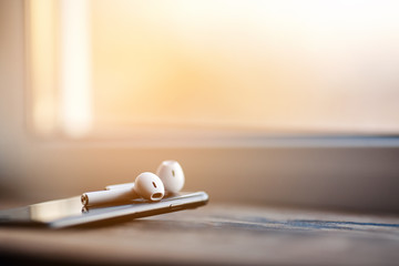 Smartphone and wireless earphones, close up isolated on the wooden background. 