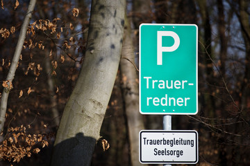  A parking lot sign at the forest in German with the words: bereavement speaker and a white sign...
