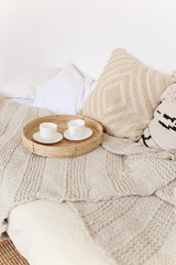 Fototapeta na wymiar Cozy bedroom decor, a pair of white cups on a wooden bed, beige bedspread and blanket, comfort, cosiness, hugge, flat lay
