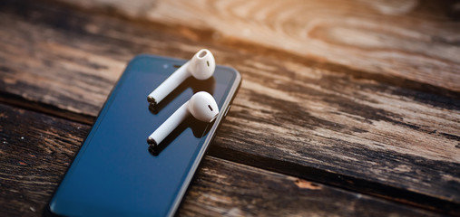 Smartphone and wireless earphones, close up isolated on the wooden background. 