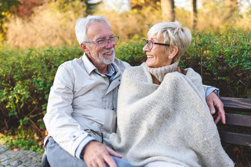Smiling senior couple sitting on the bench in the park together enjoying retirement