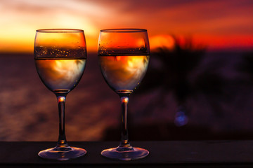 Two glasses of wine sitting on a ledge over looking the beach, ocean and a beautiful sunset.