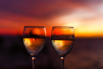 Two glasses of wine sitting on a ledge over looking the beach, ocean and a beautiful sunset.