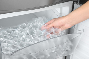 Woman taking plastic bag with ice cubes from fridge, closeup