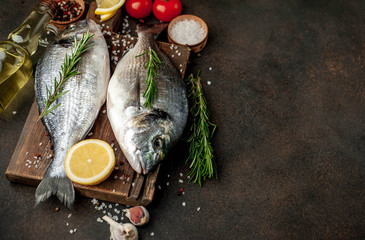 Fresh dorado fish with spices and ingredients tomato, razmorin, sunflower oil, lemon for cooking on a stone background with copy space for your text