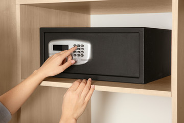 Woman opening black steel safe with electronic lock at hotel, closeup - obrazy, fototapety, plakaty