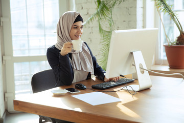 Working online. Portrait of a beautiful arabian businesswoman wearing hijab while working at openspace or office. Concept of occupation, freedom in business area, leadership, success, modern solution.