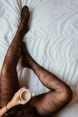 Woman sitting in bed and drinking coffee. Top view 